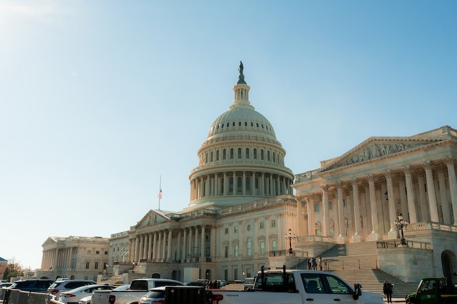 Cars park along the street in front of the U.S. Capitol as warm late-afternoon sunlight illuminates the dome and columns.